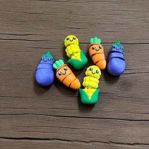May include: A collection of colorful, handcrafted vegetable-shaped figurines. The set includes smiling corn, carrots, and eggplants, each with distinct features and vibrant colors. These charming miniatures are likely decorative items or toys.