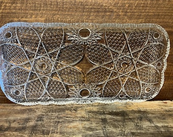 May include: A clear glass serving tray with a decorative, geometric pattern. The tray has a scalloped edge and is perfect for serving snacks or appetizers.