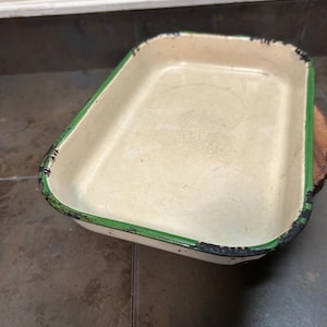 May include: A white enamel baking dish with a green rim. The dish has a rectangular shape and is slightly worn.