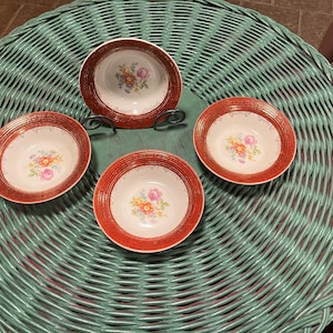 May include: Four red and white floral patterned bowls with gold trim are arranged on a green wicker surface.