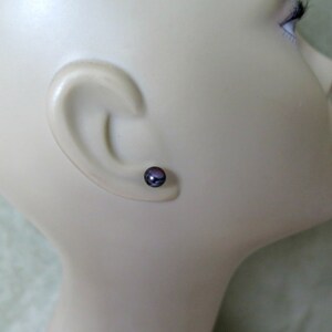 Puede incluir: Primer plano de la oreja de un maniqu&iacute; con un peque&ntilde;o pendiente de perla de color morado oscuro.