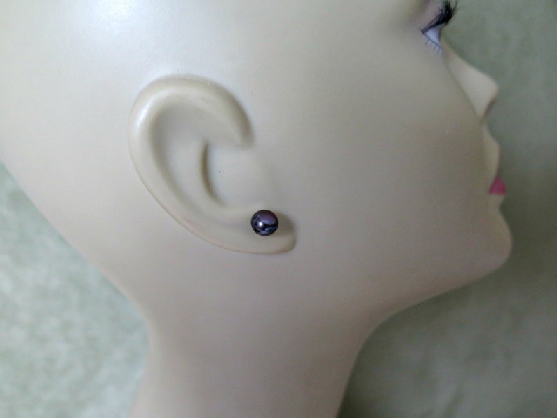 Puede incluir: Primer plano de la oreja de un maniqu&iacute; con un peque&ntilde;o pendiente de perla de color morado oscuro.