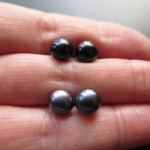 Puede incluir: Dos pares de pendientes de perlas negras en una mano.