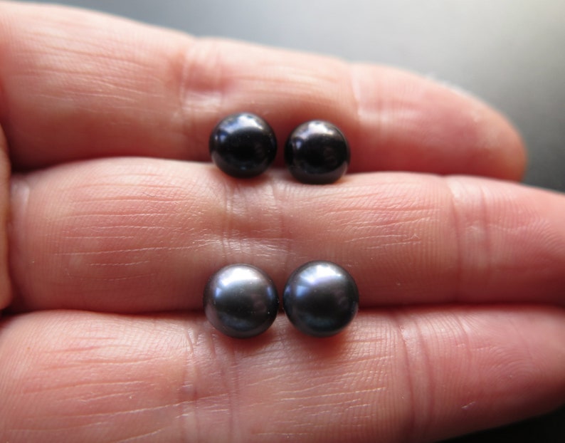 Puede incluir: Dos pares de pendientes de perlas negras en una mano.