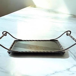 May include: Rectangular metal serving tray with decorative handles. The tray has a clear glass surface with a floral design. The handles are curved and twisted, adding a vintage touch to the tray.
