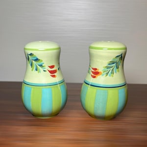 May include: A pair of ceramic salt and pepper shakers featuring a light green base with vertical stripes in lime green and turquoise. The upper section is pale green, decorated with hand-painted blue leaf patterns and small red petal accents.