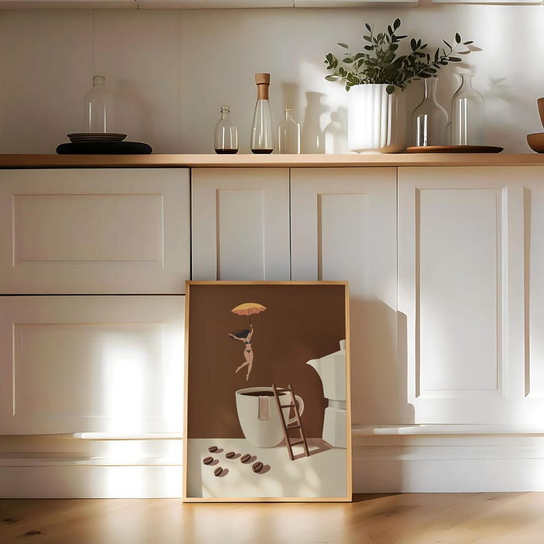 May include: A framed art print featuring a whimsical illustration of a person floating above a coffee cup with an umbrella. The artwork has a brown background, a white coffee cup, and a small wooden ladder. Coffee beans are scattered in front.