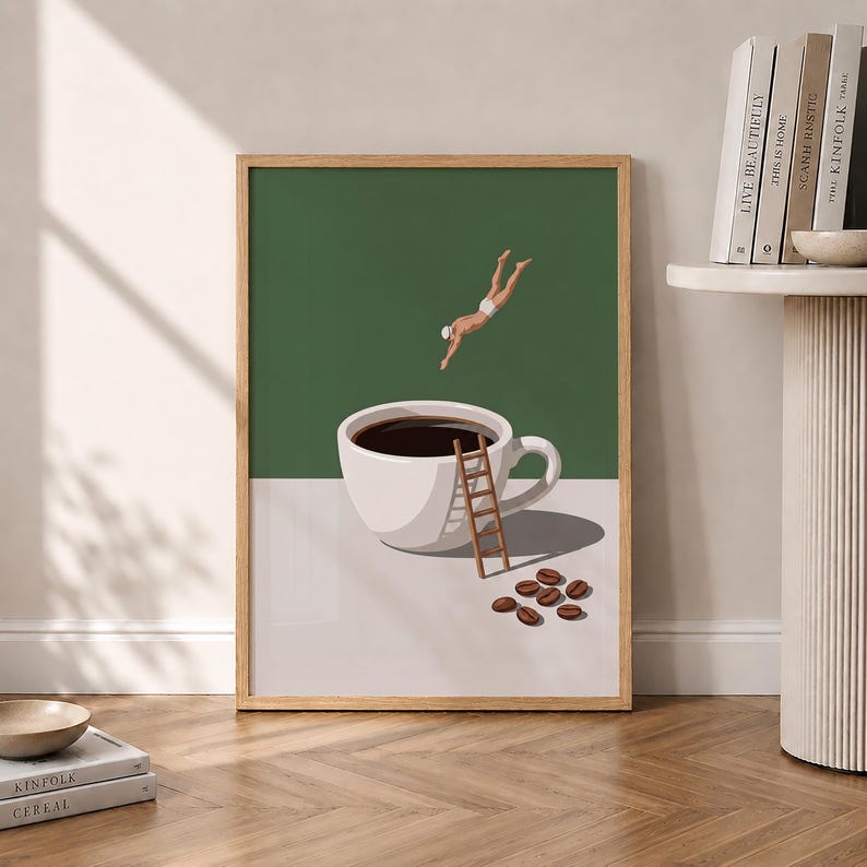 May include: A framed wall art print featuring a white coffee cup filled with dark liquid against a two-tone green and white background. A small figure in white swimwear dives towards the cup, while a wooden ladder leans against it near coffee beans.