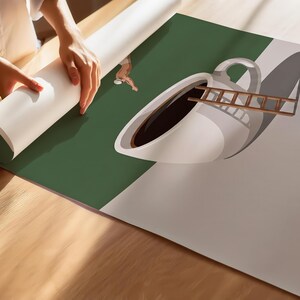 May include: A large poster print featuring a surreal graphic illustration of a white coffee cup filled with dark liquid, a wooden ladder leaning into the cup, a small figure diving into the coffee, and several scattered brown coffee beans.