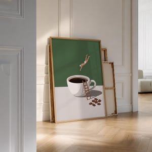 May include: A framed wall art print featuring a white coffee cup filled with dark liquid on a light surface. A small figure in white swimwear dives into the cup, while a wooden ladder leans against the side. Several coffee beans lie nearby.
