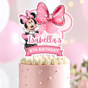 Könnte beinhalten: Ein rosa Kuchen, gekrönt von einem Minnie-Maus-Themen-Kuchenaufsatz. Der Aufsatz zeigt Minnie Maus, eine große rosa Schleife und den Text "Isabellas 8. Geburtstag" auf einem rosa Banner. Der Kuchen ist mit weißem Zuckerguss und kleinen weißen Perlen verziert.