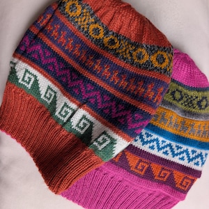 Peut inclure: Deux bonnets tricotés avec des motifs géométriques colorés. L'un est principalement orange avec des accents violets, verts et blancs. L'autre est rose avec des motifs bleus, oranges et verts. Les deux ont un bord côtelé.