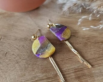 May include: A pair of gold earrings with purple and yellow resin teardrop-shaped pendants and gold tassel chains.