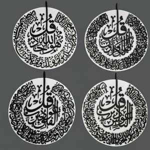 May include: Four white circular wall art pieces with black Arabic calligraphy. Each piece has a central design surrounded by smaller script. A black loop extends from the top of each piece for hanging. The background is a solid gray.