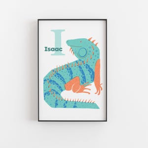 May include: A framed print featuring a teal iguana illustration. The iguana is decorated with blue and orange accents. The letter "I" and the name "Isaac" are printed in teal and dark teal, respectively, on a white background.