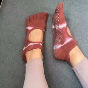 May include: Pair of maroon toe socks with a white tie-dye pattern. The socks have a cutout on the top of the foot and a non-slip grip on the sole. Designed for yoga or Pilates.