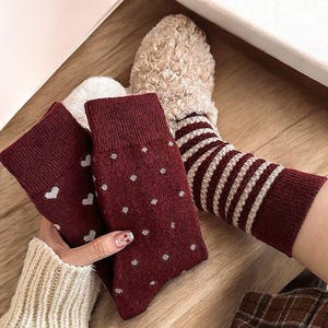 May include: Three pairs of red socks with white patterns. One pair has white polka dots, one pair has white stripes, and one pair has white hearts.