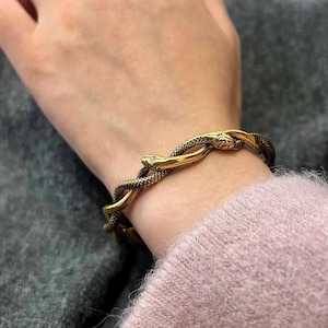 May include: A gold snake bracelet with a textured finish. The bracelet is made of two snakes intertwined together.
