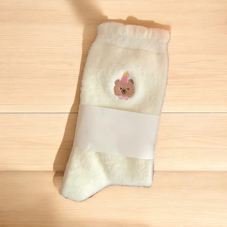 May include: White fluffy socks with a brown bear wearing a pink party hat embroidered on the front.