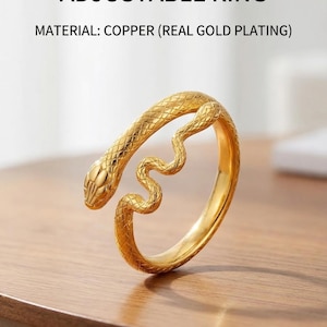 Può includere: Anello regolabile a forma di serpente placcato oro. Realizzato in rame con vera placcatura in oro. Il design del serpente si avvolge attorno al dito. L'anello è esposto su una superficie di legno. Il testo dice: Anello Regolabile Serpente Placcato Oro.