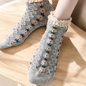 May include: A pair of gray ankle socks with a white daisy pattern and a lace trim. The socks are made of a soft, comfortable material.
