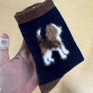Pu&ograve; includere: Calzini blu navy con polsini e punte marroni. I calzini presentano un disegno di cane soffice marrone e bianco sul davanti. I calzini sono realizzati in un materiale morbido.
