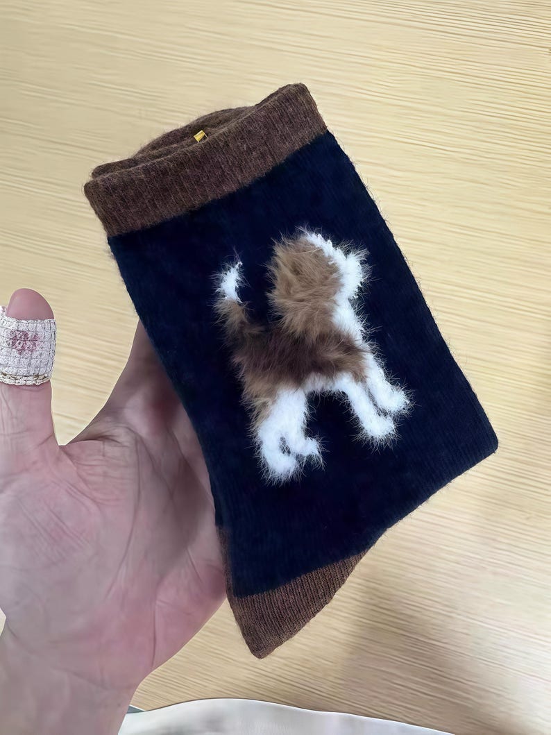 Pu&ograve; includere: Calzini blu navy con polsini e punte marroni. I calzini presentano un disegno di cane soffice marrone e bianco sul davanti. I calzini sono realizzati in un materiale morbido.