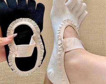 May include: A pair of toe socks, one black and one white, with a delicate ruffle trim. The black sock is held up, while the white sock is worn on a foot. Both socks have a strap across the top of the foot.