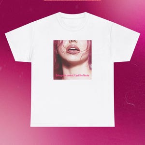 Può includere: Una t-shirt bianca a maniche corte con una grafica quadrata centrale che mostra la parte inferiore del viso di una persona con labbra e capelli dai toni rosa. Il testo "Babygirl in control, I feel like Nicole" è stampato in rosa.