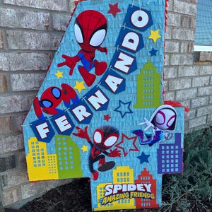 Może przedstawiać: Pi&ntilde;ata w kształcie cyfry cztery w kolorze niebieskim i czerwonym z motywem Spidermana. Pi&ntilde;ata ma baner z napisem "Fernando" i logo Spidermana z napisem "Spidey Amazing Friends".
