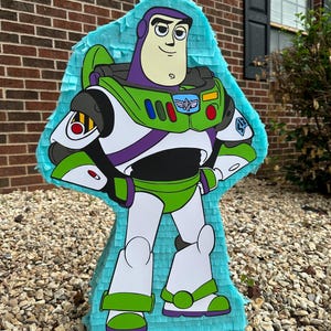 May include: A blue and green Buzz Lightyear pi&ntilde;ata with a white background. The pi&ntilde;ata is made of tissue paper and has a string attached to the top.