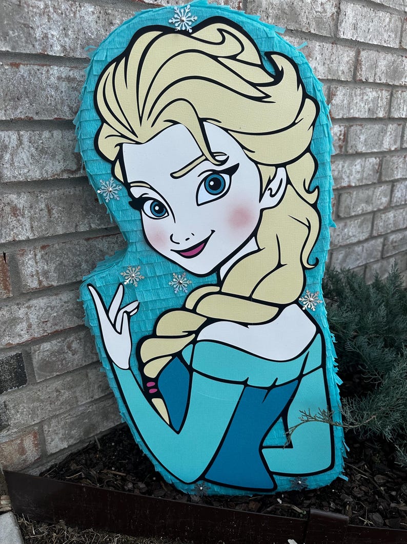 Puede incluir: Una pi&ntilde;ata azul y blanca con forma de Elsa de la pel&iacute;cula Frozen. La pi&ntilde;ata tiene una cara detallada con ojos azules y un rubor rosado. Elsa lleva un vestido azul con un cuello blanco y una trenza en el pelo.
