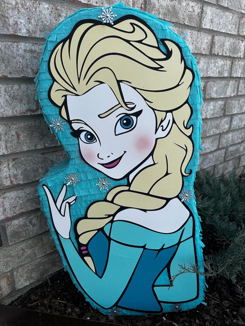 Puede incluir: Una pi&ntilde;ata azul y blanca con forma de Elsa de la pel&iacute;cula Frozen. La pi&ntilde;ata tiene una ilustraci&oacute;n detallada de la cara y el cabello de Elsa. Hay copos de nieve en la pi&ntilde;ata.