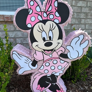 May include: A pink and black Minnie Mouse pinata with white polka dots. The pinata is shaped like Minnie Mouse and has a big bow on her head.