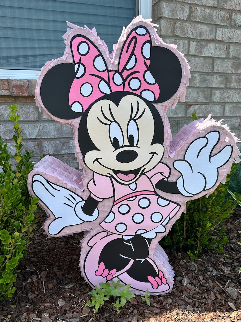 May include: A pink and black Minnie Mouse pinata with white polka dots. The pinata is shaped like Minnie Mouse and has a big bow on her head.