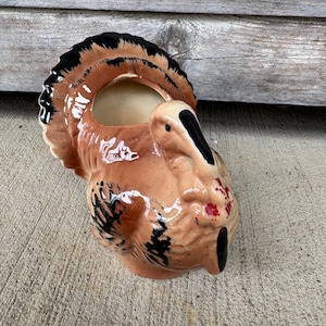 May include: A ceramic turkey-shaped planter or serving vessel featuring a glossy finish in shades of brown, tan, and black. The turkey has a prominent fanned tail, a detailed head with a black beak, and a red wattle, with a hollow opening at the top.