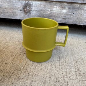May include: A solid olive green mug with a textured finish and a distinct horizontal ridge encircling the middle of the body. The mug features a square-shaped handle attached to the side, providing a sturdy grip for this functional drinkware item.