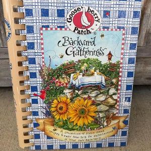 May include: A spiral-bound cookbook titled "Backyard Gatherings" with a blue and white checkered cover. The cover features a colorful illustration of a backyard scene with sunflowers, a table setting, and the text "Gooseberry Patch". The book includes recipes and entertaining ideas.