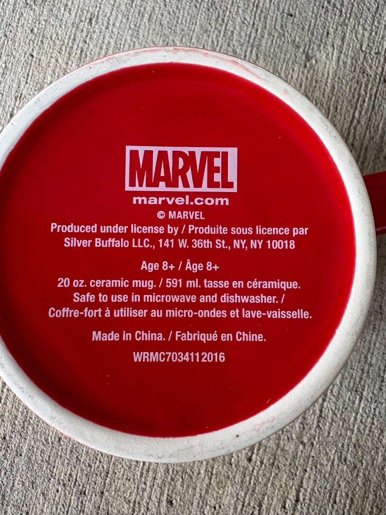 May include: A red ceramic mug with the Marvel logo and text. The mug is 20 oz. and safe for microwave and dishwasher use. The text includes the Marvel website and copyright information.