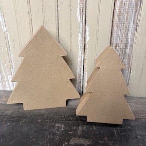 May include: Two flat, tree-shaped cutouts made of light brown, compressed fiberboard material. The larger tree stands to the left, while a slightly smaller tree is positioned to the right. Both items feature a simple, symmetrical, three-tiered design.