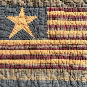 May include: A quilted textile featuring a design reminiscent of the American flag. The quilt showcases a blue field with a gold star and alternating stripes of gold and red plaid. The fabric has a textured, quilted appearance.