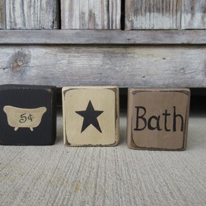 May include: Three wooden blocks with black painted edges. The first block is black with a white bathtub and the text "5¢". The second block is beige with a black star. The third block is brown with the text "Bath" in black.