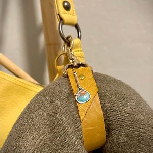 May include: A yellow leather handbag with a brown leather strap and a key charm with a turquoise stone.
