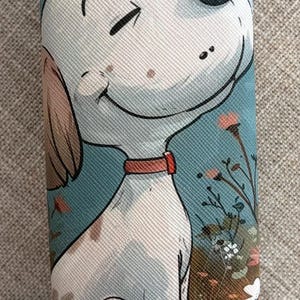 May include: A blue eyeglasses case featuring a smiling cartoon dog with a red collar, set against a backdrop of flowers. The case has a textured surface and a curved shape, ideal for protecting eyewear.