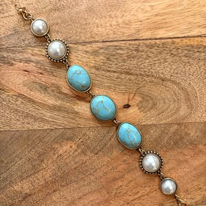 May include: Gold-toned bracelet featuring oval turquoise stones and faux pearls. The bracelet has a delicate design with a lobster clasp closure. The pearls are set in decorative settings, adding a touch of elegance.