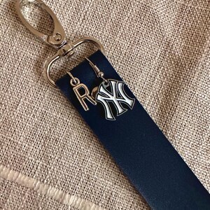 May include: A navy blue leather keychain with a silver clasp and two charms. One charm is a silver letter "R" and the other is a silver and white New York Yankees logo.