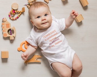 Free US shipping | Baby romper with orange and crimson text - Tennessee is undefeated by Alabama in my lifetime.  Football baby snap shirt.