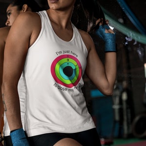 May include: White tank top with the text "I'm just here to close my rings" and a colorful graphic. The shirt is worn by a person in a gym setting, with black shorts and blue hand wraps.