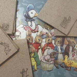Pode incluir: Uma cole&ccedil;&atilde;o de cart&otilde;es de papel kraft com ilustra&ccedil;&otilde;es estampadas de personagens de uma hist&oacute;ria infantil. O fundo apresenta uma ilustra&ccedil;&atilde;o colorida de v&aacute;rios personagens animais. Os cart&otilde;es t&ecirc;m ilustra&ccedil;&otilde;es diferentes.