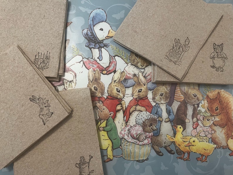 Pode incluir: Uma cole&ccedil;&atilde;o de cart&otilde;es de papel kraft com ilustra&ccedil;&otilde;es estampadas de personagens de uma hist&oacute;ria infantil. O fundo apresenta uma ilustra&ccedil;&atilde;o colorida de v&aacute;rios personagens animais. Os cart&otilde;es t&ecirc;m ilustra&ccedil;&otilde;es diferentes.